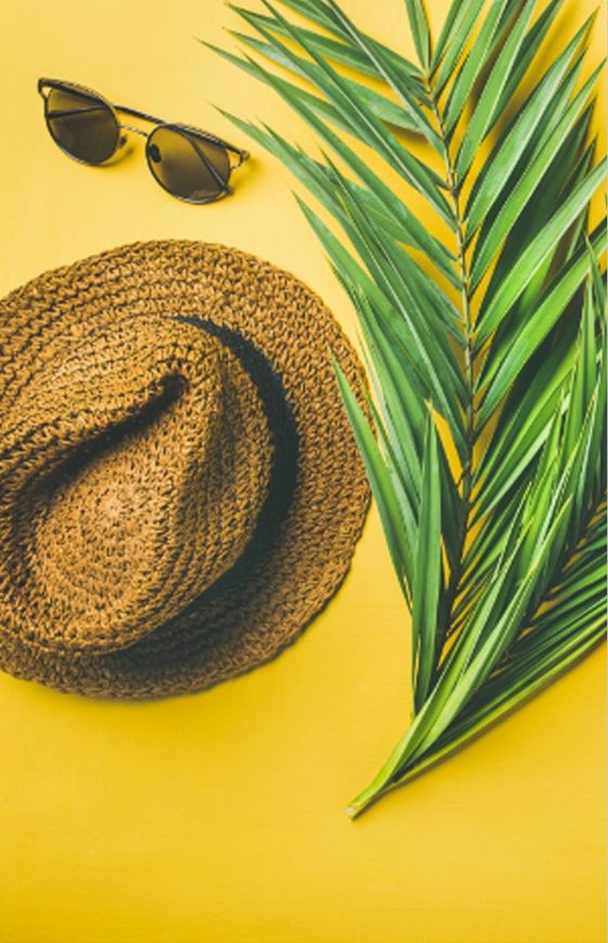 A straw hat, sunglasses, and a palm leaf on a yellow background