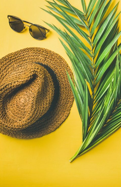 A straw hat, sunglasses, and a palm leaf on a yellow background
